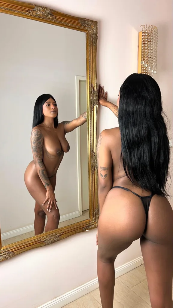 Masseurin Nina in schwarzem glänzendem Outfit mit erhobenen Armen
